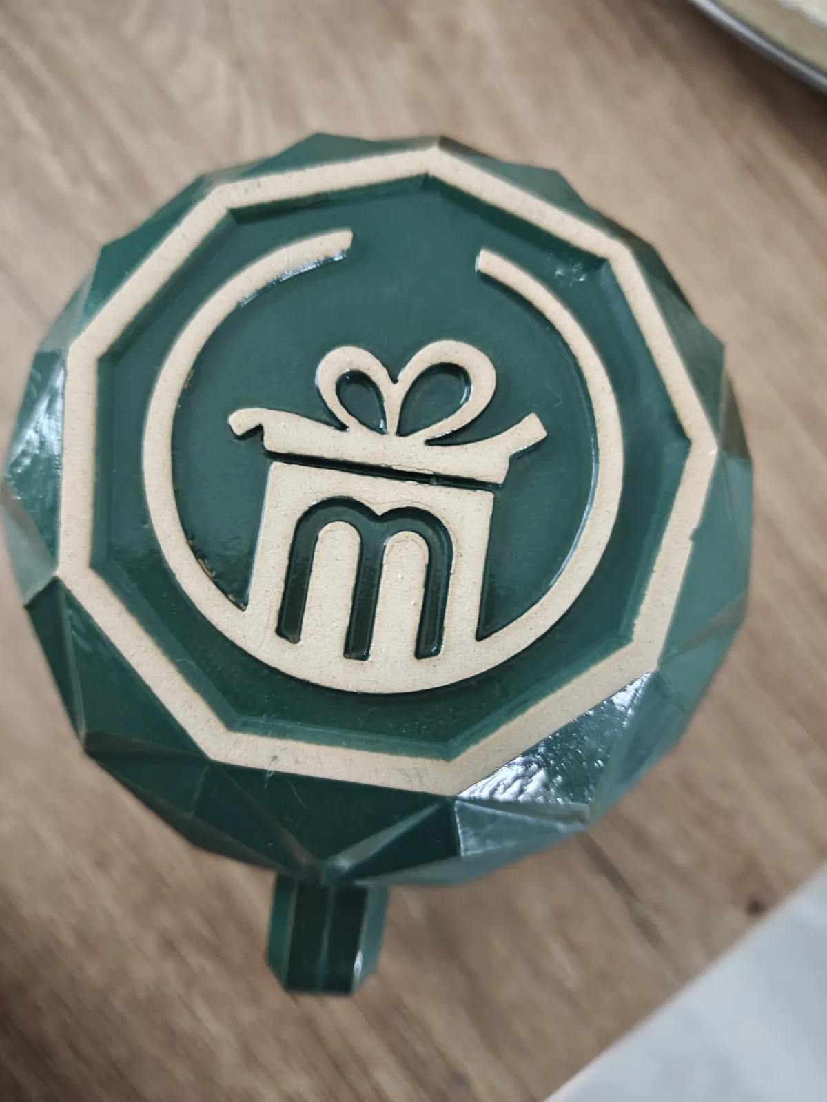 Unterseite einer dunkelgrün glasierten Tasse mit dem Miroria-„m“ im Boden.