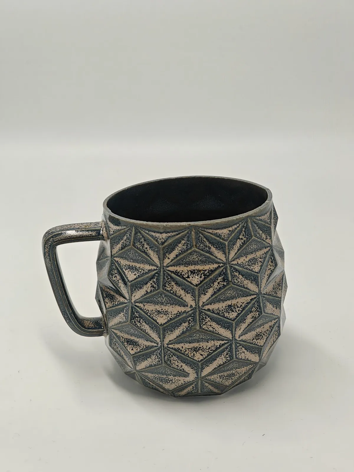 Dreieck-Tasse in einer petrolfarbenen Glasur, die auf den Facetten zu gesprenkeltem Creme aufreißt.