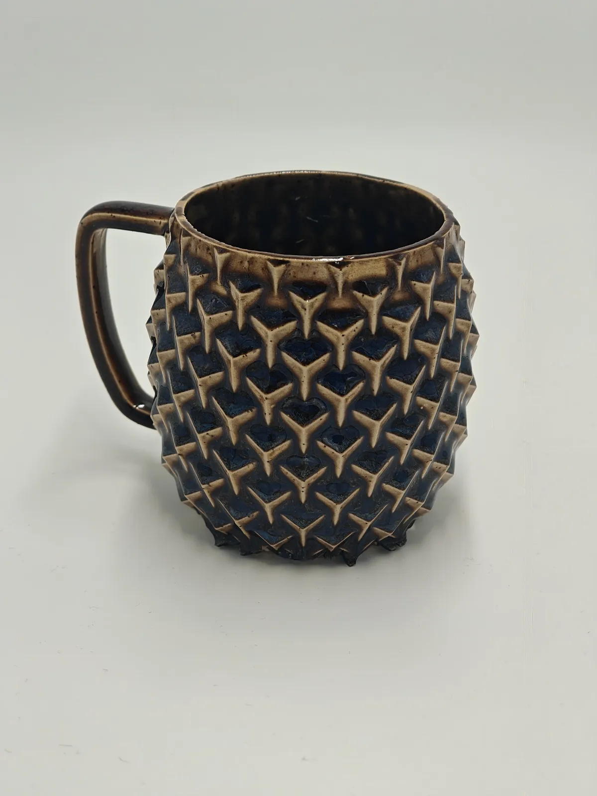 Würfel-Tasse mit dichtem Relief aus würfelförmigen Spitzen, dunkelblau glasiert mit cremefarbenen Spitzen und braunem Henkel.